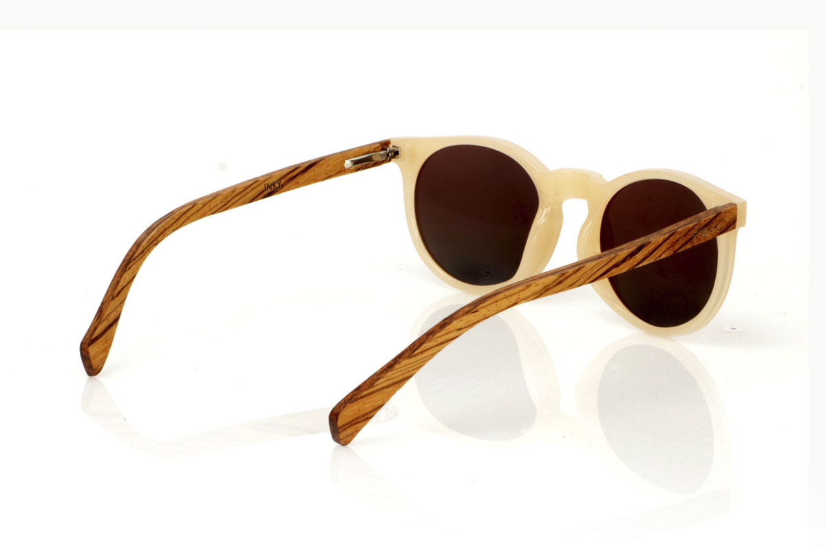 Wood eyewear of Zebrano INKY. INKY sunglasses capture the essence of a delicate and feminine design with their rounded shape and smaller size. The frame in a sophisticated satin-gloss ivory offers a touch of light and elegance, while the zebrawood temples introduce a natural and striking contrast. This model is ideal for those looking for distinctive but subtle glasses that complement without overloading. With measurements of 138x48mm and a caliber of 47, the INKY adapts perfectly to thinner faces, ensuring comfort and style. Immerse yourself in the beauty of the details to enhance your look with a unique charm. for Wholesale & Retail | Root Sunglasses® 